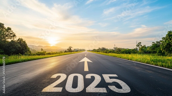 Fototapeta A wide, empty road stretching into the distance, with the bold numbers "2025" painted on the asphalt, a large arrow pointing to the horizon where a sunrise breaks through the cloud