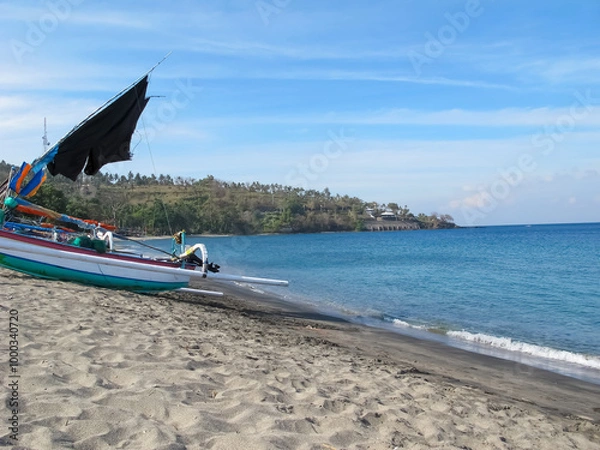 Obraz Coastal beach with a stretch of white sand on a cape, featuring a few anchored boats and a scenic view of a forest lining the shoreline