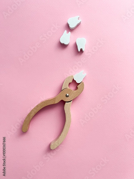 Fototapeta White wooden teeth and forceps on a pink background. Dental health concept. Dentist day concept. Top view, space for copy text