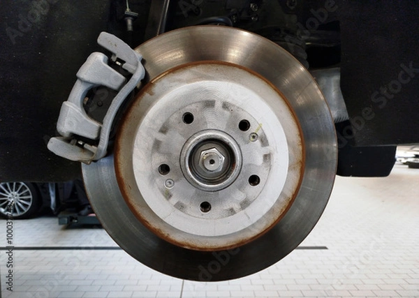 Fototapeta A brake disc and brake caliper installed on a car that is on a lift in a car service center.