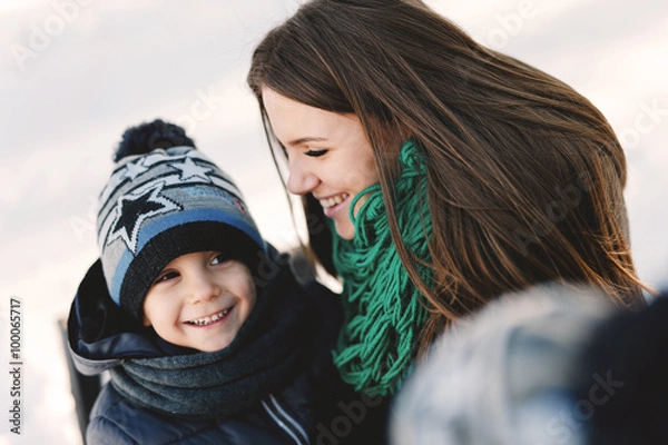 Obraz Cute young pregnant mother and her child having fun in winter park on a bright day hugging each other and smiling
