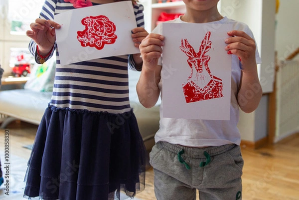 Fototapeta Children creating lino cut prints on paper using rollers, paint, and spoons in an art workshop. Creativity, craft techniques, and artistic expression, educational and creative stock imagery.