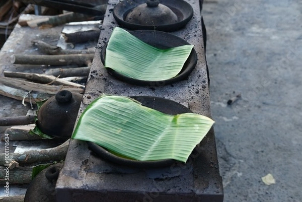 Obraz A traditional Indonesian serabi-making process, showing hands pouring batter onto a clay pan over a wood-fired stove. The smoky atmosphere and authentic tools emphasize the local street food culture.