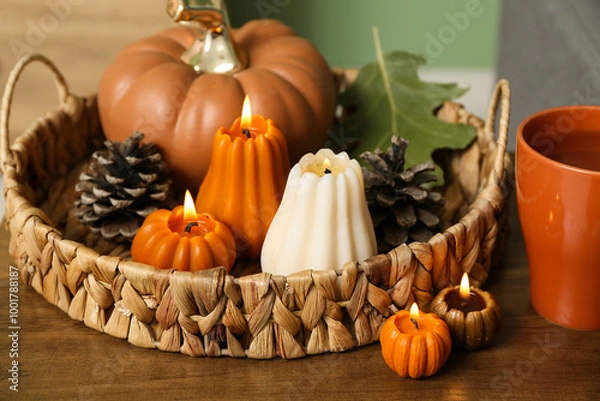 Fototapeta Wicker basket with burning candles in shape of pumpkins, forest bumps and tea cup on coffee table at home, closeup