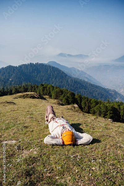 Fototapeta Man sleeping on grass with cap  enjoying natural sun bath in Valley Himachal Pradesh India.