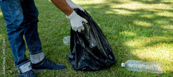 Fototapeta Hand holding plastic bottle waste, picking up trash and putting it in the black garbage bag at the Park on Environmental Earth day