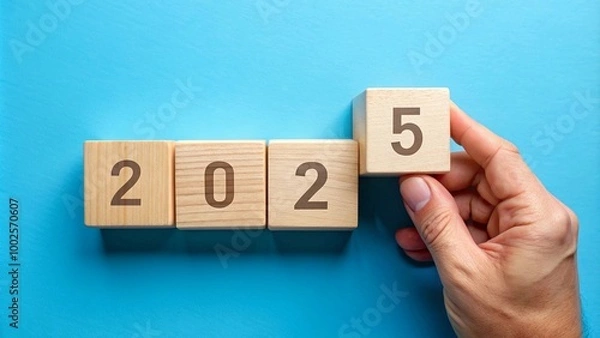 Fototapeta A hand placing wooden blocks with numbers to form 2025, symbolizing the transition to a new year and new beginnings. Perfect for concepts of change, progress and future goals.