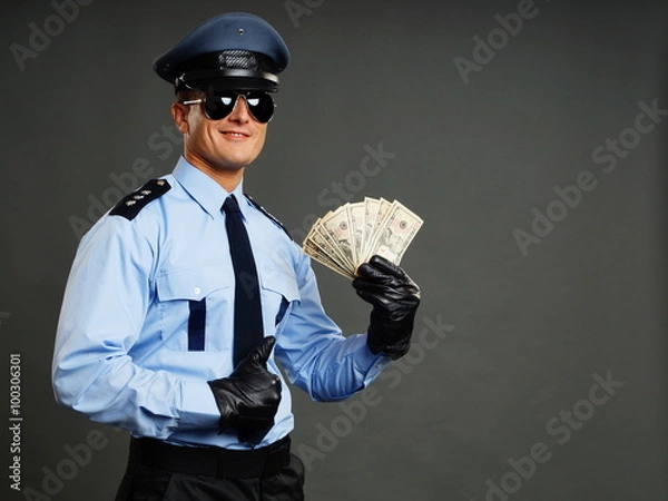 Fototapeta Policeman in uniform holds money in hands and shows thumb up