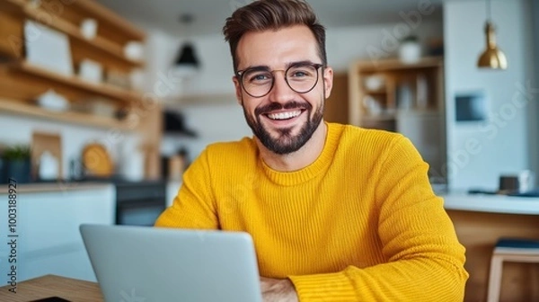 Obraz A man in a yellow sweater smiling at the camera while using his laptop, AI