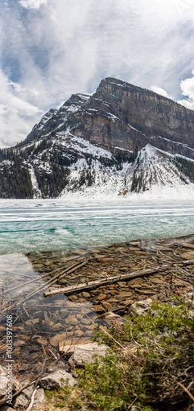 Fototapeta Incredible nature views at Lake Louise in world famous Alberta during spring time with partially frozen lake. Turquoise, aqua water colour showing through layer of ice on water surface. 
