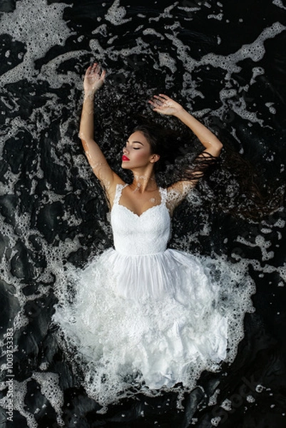 Obraz A woman with dark hair wearing a white dress and floating in the dark water