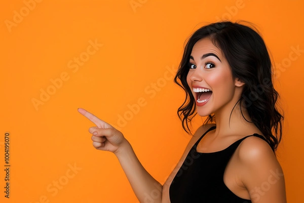 Obraz Beautiful girl posing on orange background and pointing finger at place for advertisement and text