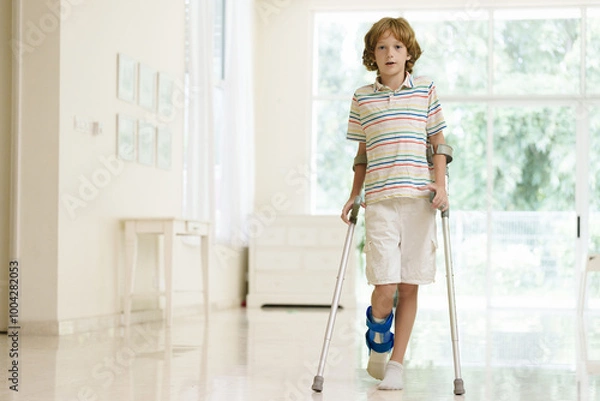Fototapeta Injured child on crutches. Boy in cast on foot