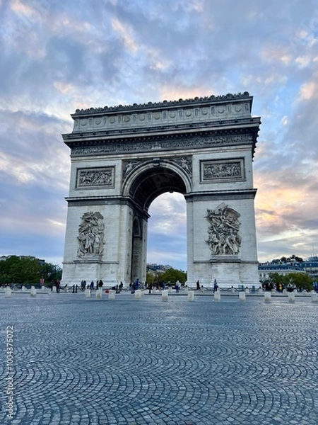 Obraz The Arc de Triomphe in Paris during the day with a dramatic, partly cloudy sky.  No cars, unrecognisable people in the background. 