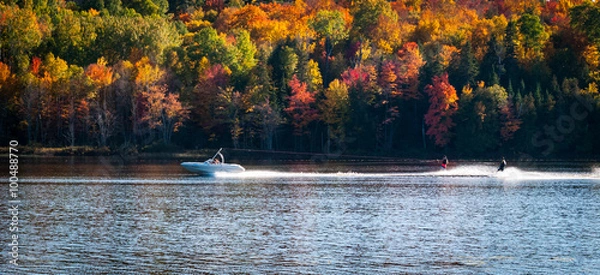 Fototapeta Late summer on a northern Ontario lake - getting in the last session of water skiing.  A boat speeding along pulls a pair of water skiers.  Have fun on one of the last warm days of summer.  