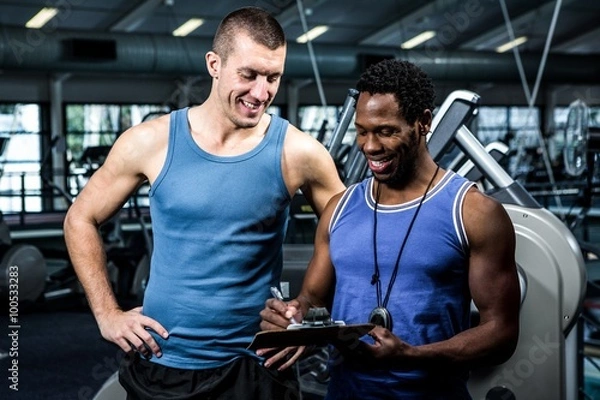 Fototapeta Muscular man discussing performance with trainer 