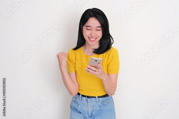 Fototapeta A woman clenched fist showing happy expression when looking at his mobile phone