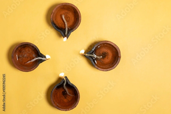 Fototapeta Happy Diwali - Overhead view of glowing clay diyas on vibrant yellow background with space for text