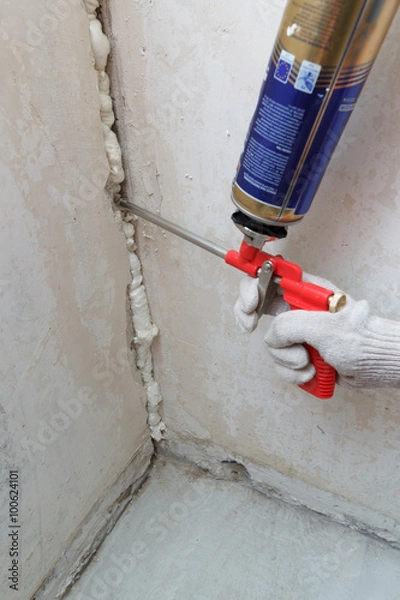 Fototapeta Worker's hand fix a rent in wall using polyurethane foam