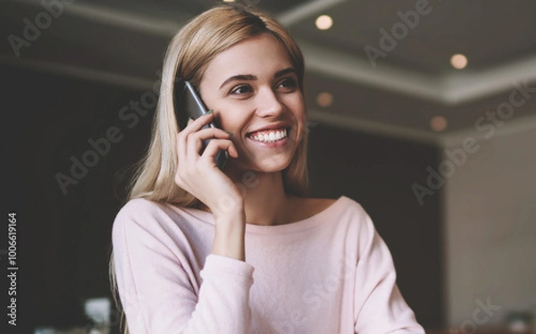 Fototapeta Positive female student calling to friend for discussing details about university task for course work, happy woman using mobile application for making conversation during learning in classroom