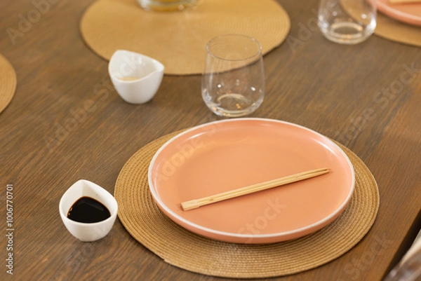 Obraz Chopsticks on pink plate with soy sauce and glass on dining table