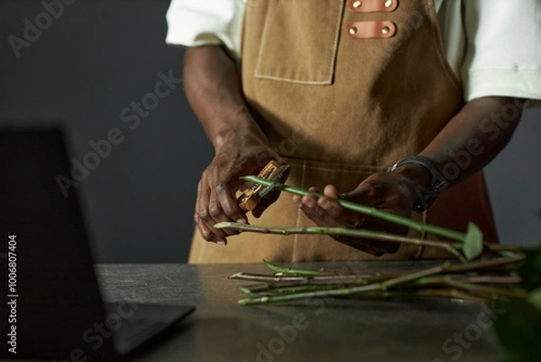 Fototapeta Minimal closeup of male florist arranging bouquet and cutting flower stems in low lighting copy space