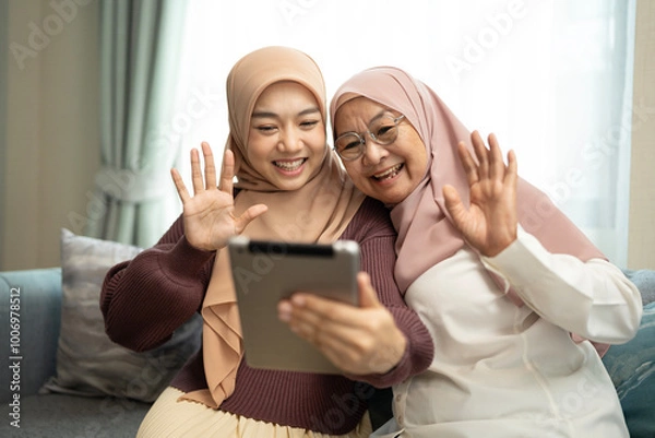 Fototapeta Muslim mother and daughter using tablet making video call in a living room