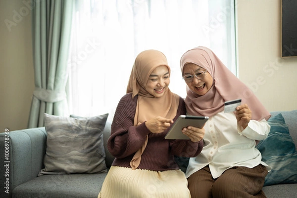 Fototapeta Happy muslim mother and daughter shopping online with digital tablet in a living room