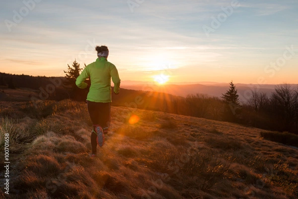 Obraz woman from back running on the trail in the mountains with first ray of light in the morning