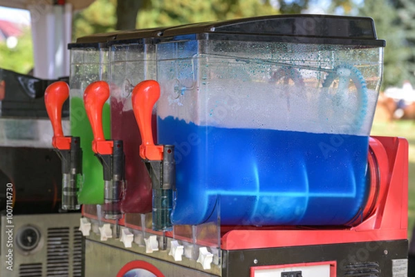 Obraz Slush machine making colorful frozen drinks with different flavors, refreshing beverages with ice in blue, red and green at a funfair market