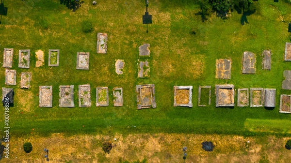 Fototapeta Aerial view of a serene cemetery with a patchwork of tombstones casting shadows over the lush grass, evoking a sense of peaceful finality