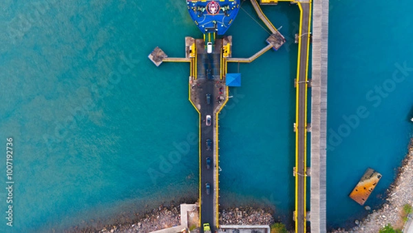 Fototapeta Aerial view of a vibrant ferry dock showcasing the dynamic interplay of bold colors and geometric arrangement between ship, sea, and infrastructure