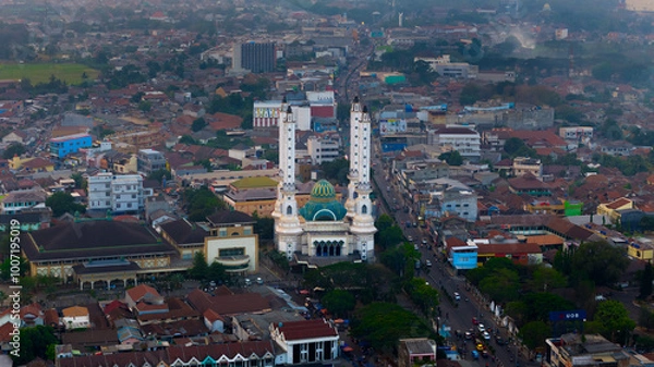 Obraz Aerial view of a bustling city street leading towards an iconic mosque with tower amid a sprawling urban landscape at dusk