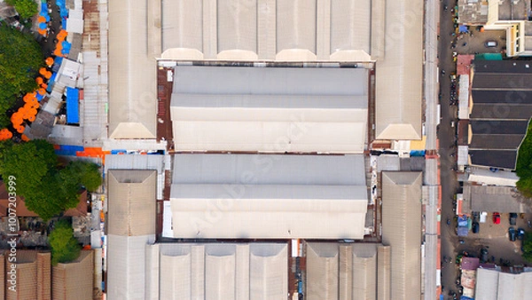 Fototapeta Top-down view capturing the intricate patterns and symmetry of industrial warehouse roofs, surrounded by urban life