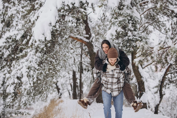 Fototapeta A young happy and loving couple is having fun in a snowy forest in winter.