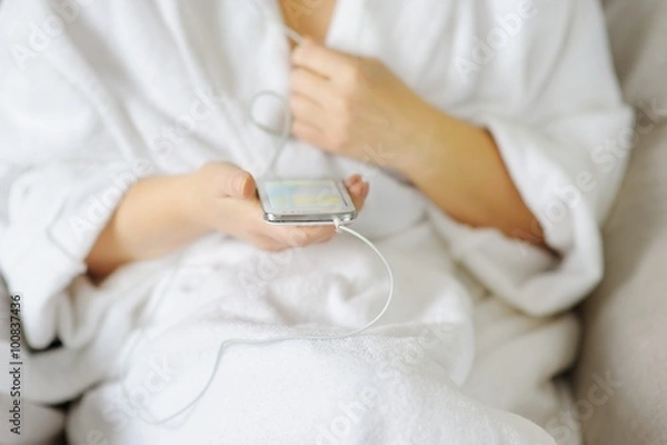 Fototapeta A woman in a white coat chooses the music on your smartphone.