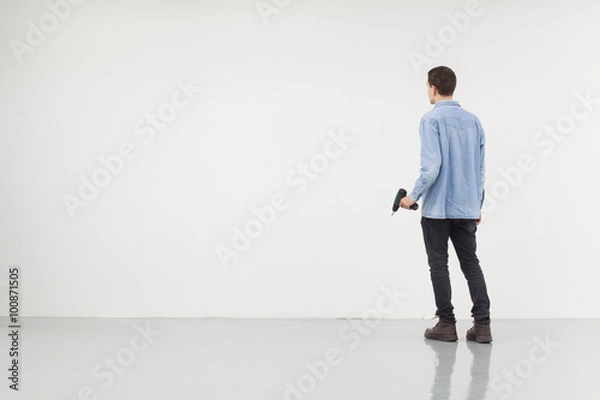 Obraz Man holding a drilling machine standing in front of a white wall