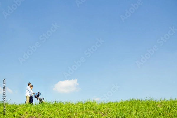 Fototapeta 青空の下、土手でベビーカーを押す夫婦