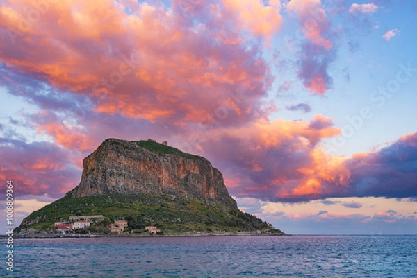 Fototapeta Dramatic sunset illuminating Monemvasia and its rocky coastline in Greece. The sky above is bursting with vibrant colors as the sun sets over the mediterranean sea