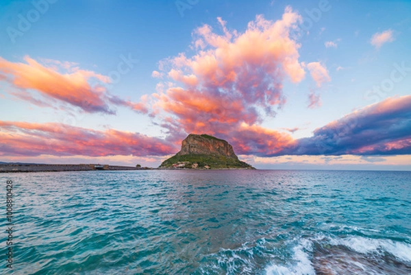 Fototapeta Dramatic sunset illuminating Monemvasia and its rocky coastline in Greece. The sky above is bursting with vibrant colors as the sun sets over the mediterranean sea