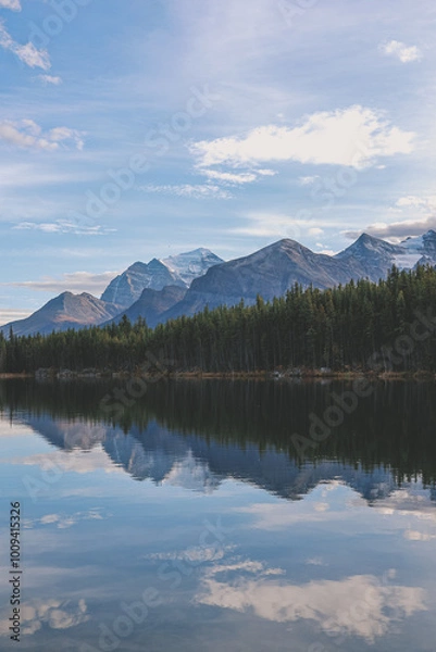 Fototapeta A serene mountain lake reflects a clear blue sky and snow-capped peaks. Lush green forests line the shoreline. The tranquil scene is perfect for relaxation, with the calm waters and majestic mountains