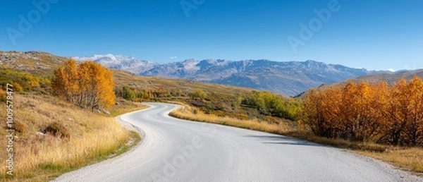 Fototapeta  A road with a curved section, surrounded by a grassy area, leads to a mountain range in the background