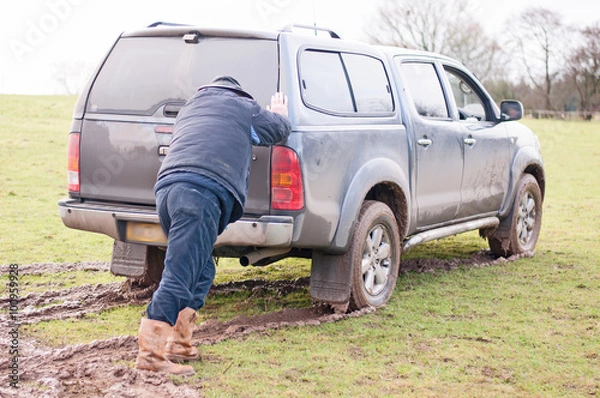 Fototapeta Man assisting a vehicle that is stuck in the mud