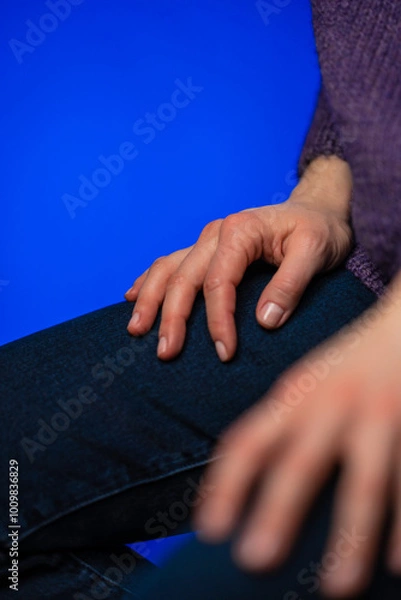 Fototapeta A female sitting on a chair in purple knitted sweater hands are on her laps. Woman's hands are down. Feeling powerless in some circumstances.