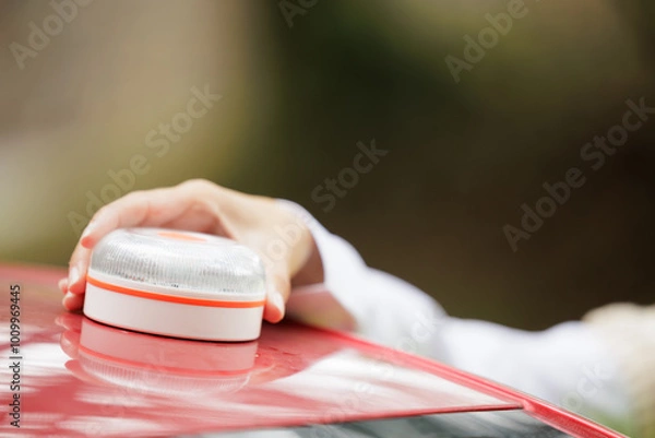 Obraz Young woman with reflective vest, places the V16 emergency light beacon on the roof of the damaged vehicle. Help flash, mandatory to replace triangles in Europe. DGT Spain.