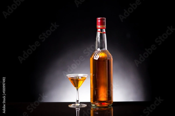 Fototapeta red wine glass and a wine bottles in black background