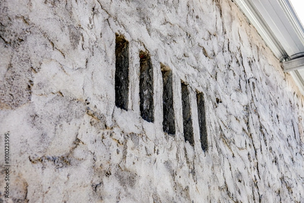 Obraz Close-up of a textured stone wall with vertical slits, creating a unique architectural detail that combines rustic and minimalist elements, perfect for backgrounds or design use