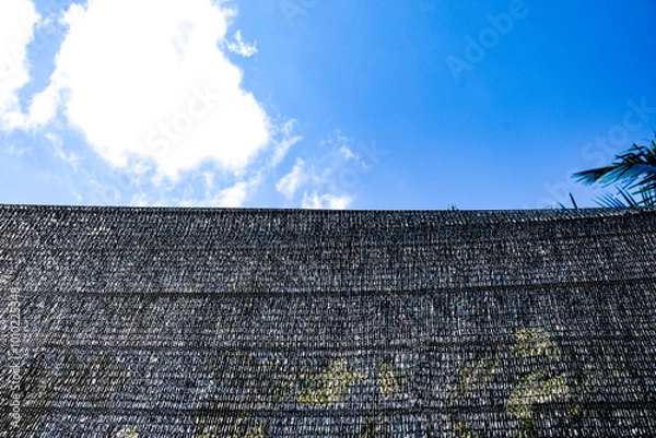 Obraz Paranet plastic mesh against a bright blue sky, creating a contrast between industrial texture and natural elements, ideal for backgrounds, outdoor scenes, or design concepts