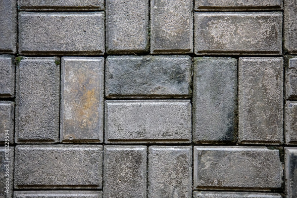 Obraz A textured close-up background of a wet brick pavement with a geometric, interlocking pattern, highlighting the rough surface and subtle reflections of light