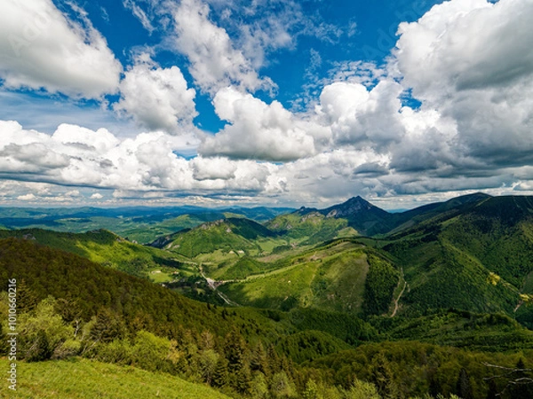 Fototapeta View of the Rozsutec mountain in the Mala Fatra mountains in Slovakia. The vast landscape features rolling green hills, dense forests, and a dramatic sky filled with large, bright clouds on a clear da